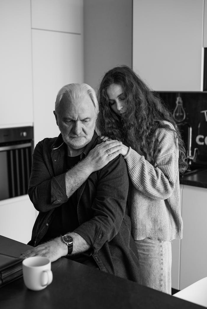 Black and white photo of an elderly man and woman indoors expressing sorrow.
